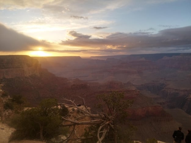 A panoramic view of the Grand Canyon during sunrise in late October, with fewer people visible compared to a typical summer day. The colors of the canyon are vibrant, and the light is soft and golden.