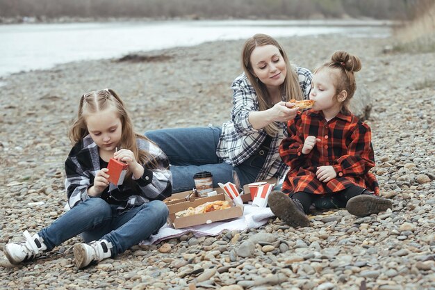 A family preparing a picnic lunch at a scenic overlook in Yellowstone National Park, with a geyser erupting in the background. They are using reusable containers and water bottles to minimize waste.
