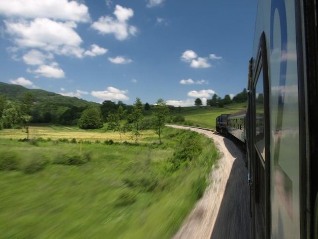 A scenic shot of a high-speed train passing through a green, rural landscape, emphasizing the environmental benefits and sustainability of rail travel. Include elements like trees, fields, and wind turbines.