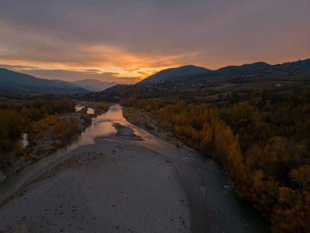 A landscape photo taken during the golden hour, showing rolling hills and a winding river bathed in warm, golden light. The sky is clear with a few soft clouds, and the overall scene is vibrant and inviting.
