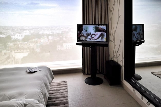 A luxurious hotel room with a king-size bed, a view overlooking a city skyline, and amenities like a flat-screen TV, a mini-fridge, and a coffee maker.