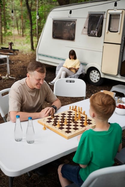 Close up of a travel-sized board game being played on a small table inside a camper van. Hands are visible, showing pieces being moved on the board.