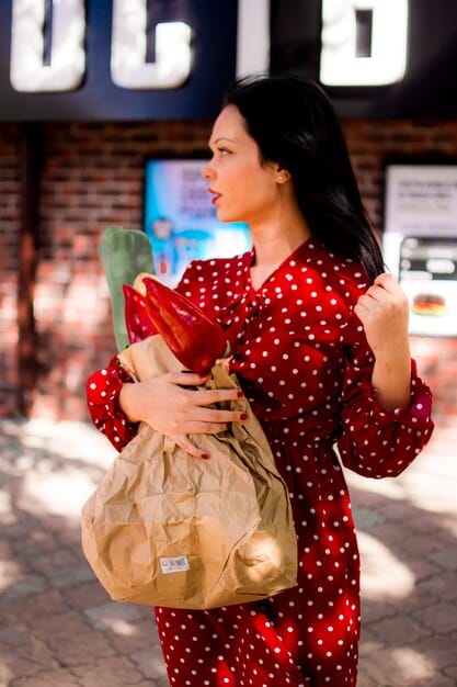 A traveler at a local market in the US, using reusable shopping bags and produce sacks to carry their fresh produce and souvenirs. The scene highlights sustainable shopping practices while traveling.