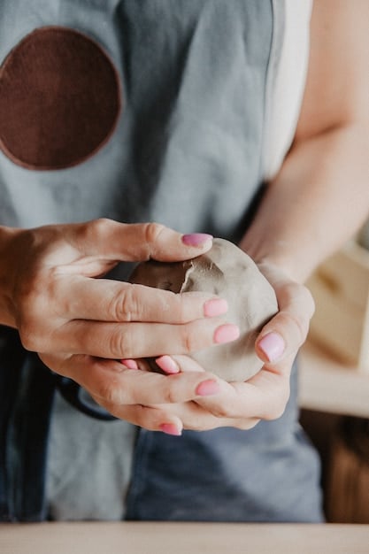 An artisan's hands carefully shaping clay on a pottery wheel in a brightly lit studio. Shelves lined with finished ceramic pieces are visible in the background, showcasing a range of styles and colors.