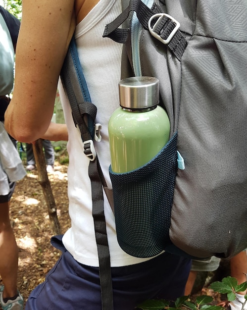 A close-up of a traveler's backpack showcasing various reusable items: a stainless steel water bottle, bamboo cutlery set, reusable shopping bag, and beeswax food wraps.