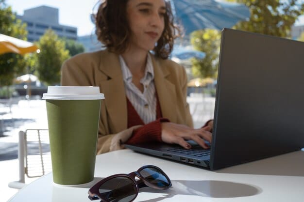 A blogger working on a laptop at a cafe, surrounded by travel guides and a cup of coffee. The laptop screen shows an article about affordable travel insurance options.