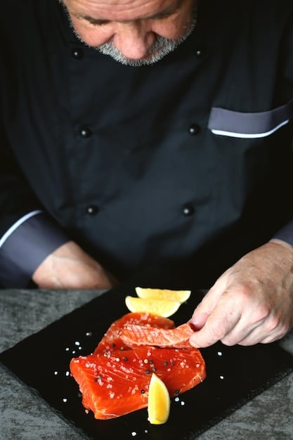 A close-up shot of a chef preparing a gourmet meal in a cruise ship kitchen. The kitchen is modern and spotless, with gleaming stainless steel surfaces and an array of fresh ingredients. Other chefs and culinary staff are visible in the background, working efficiently.