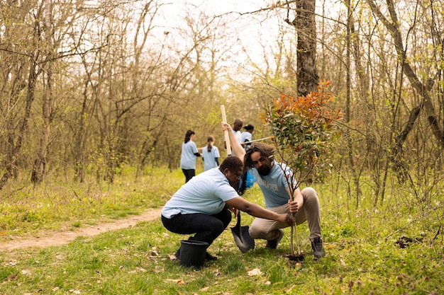 A group of tourists participating in a tree-planting activity in a deforested area. The tourists are smiling and working alongside local community members. The backdrop includes a reforestation project with saplings and young trees.