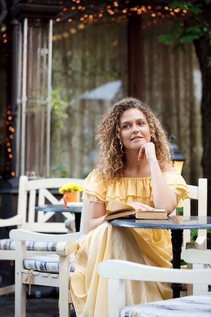 A woman sitting at an outdoor cafe in a European city, sipping coffee and reading a book. She looks relaxed and content.