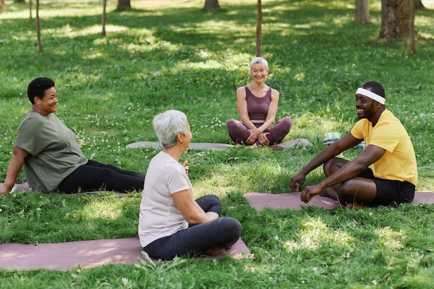 A group of people participating in a guided meditation session outdoors, sitting in a circle on a grassy field with a clear blue sky above. The scene conveys a sense of community and emotional connection.