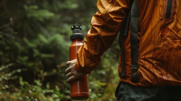 A close-up shot of a traveler using a reusable water bottle while hiking in a national park. The background shows a clear mountain stream and lush greenery.