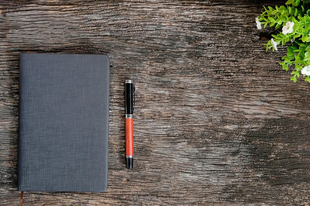 A close-up, top-down view of a notebook and pen on a wooden table, surrounded by travel brochures and a cup of coffee. The open notebook has the words 